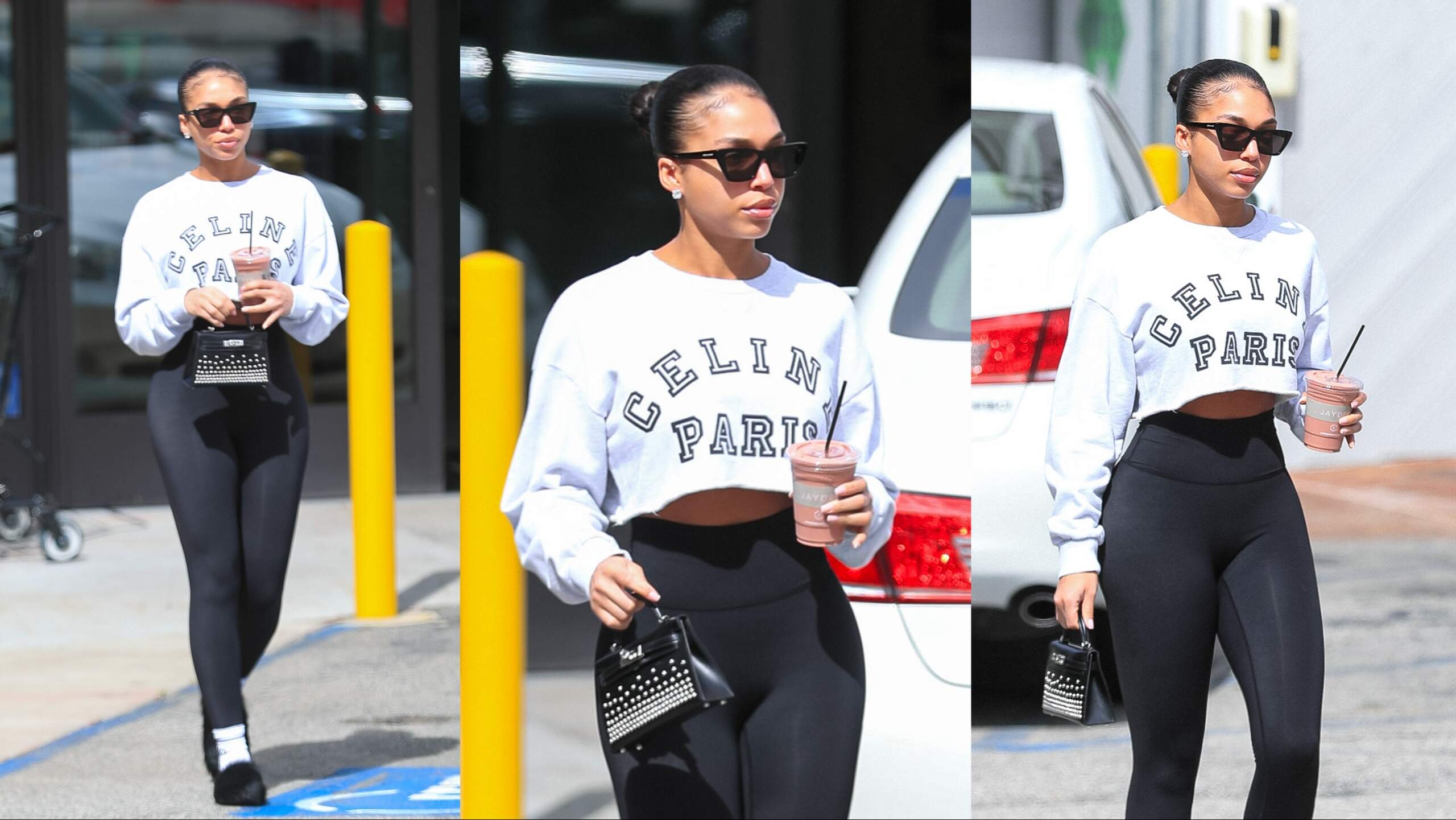 Model Lori Harvey carries a smoothie after working out in black leggings and a gray cut-off sweatshirt