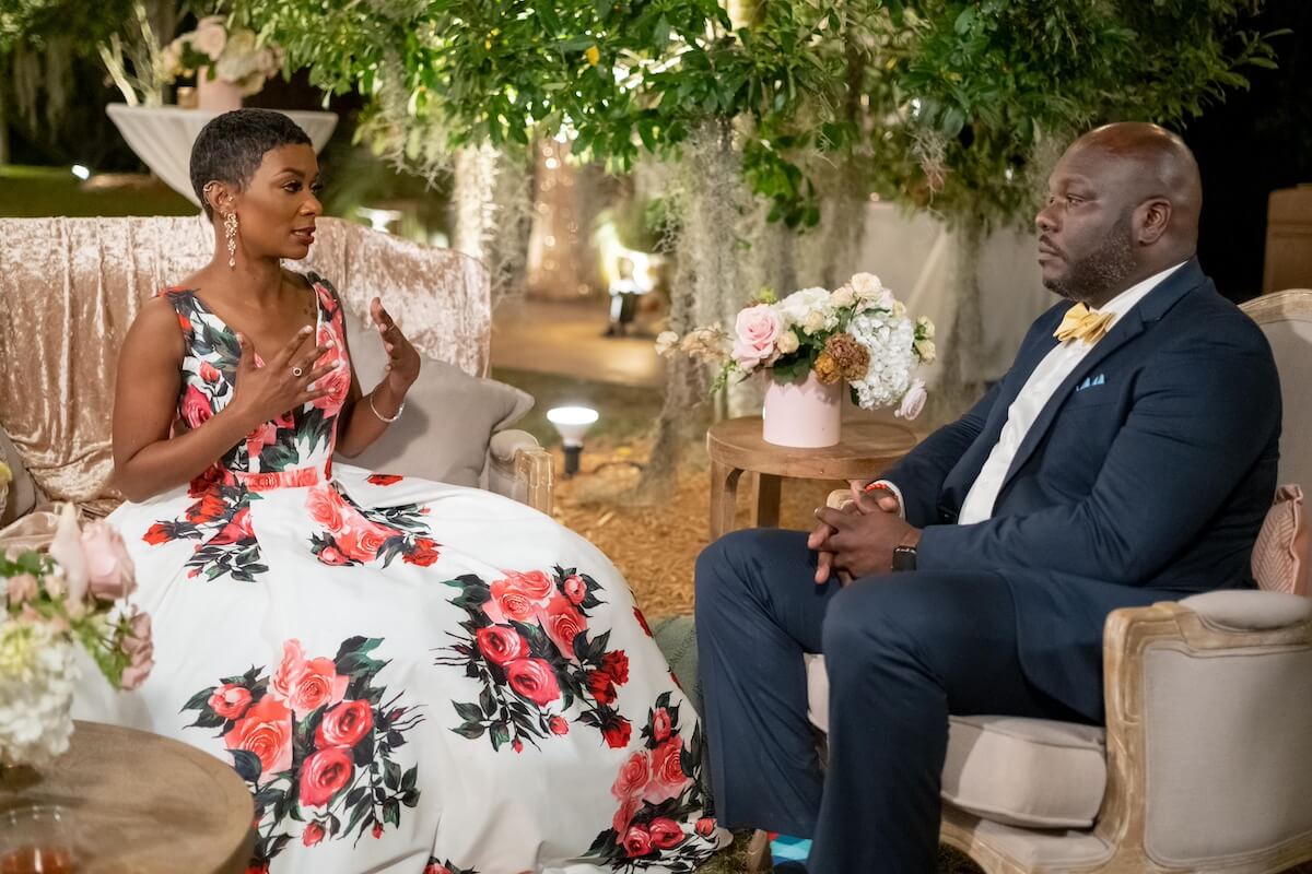 A Black woman in a floral dress talking to a Black man in a suit