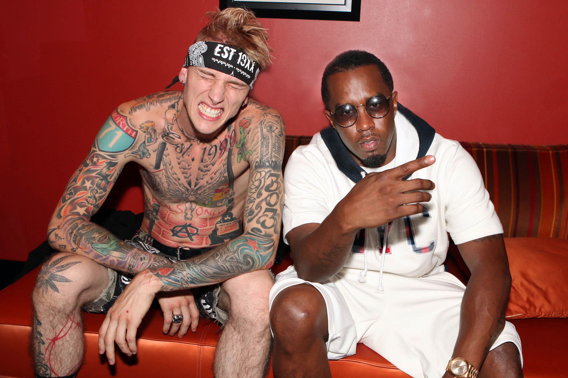 Machine Gun Kelly sitting shirtless and smiling next to Sean 'P. Diddy' Combs