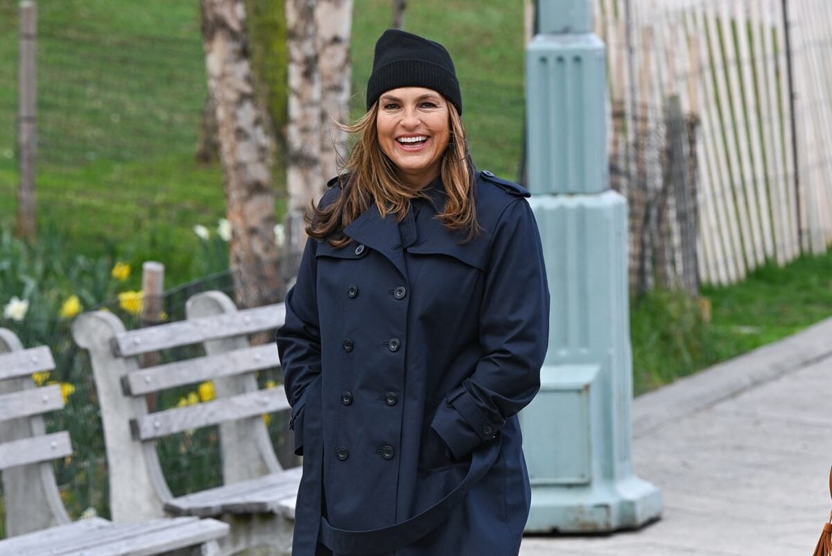 Mariska Hargitay smiling while wearing a trench coat on the set of 'Law & Order SVU'.