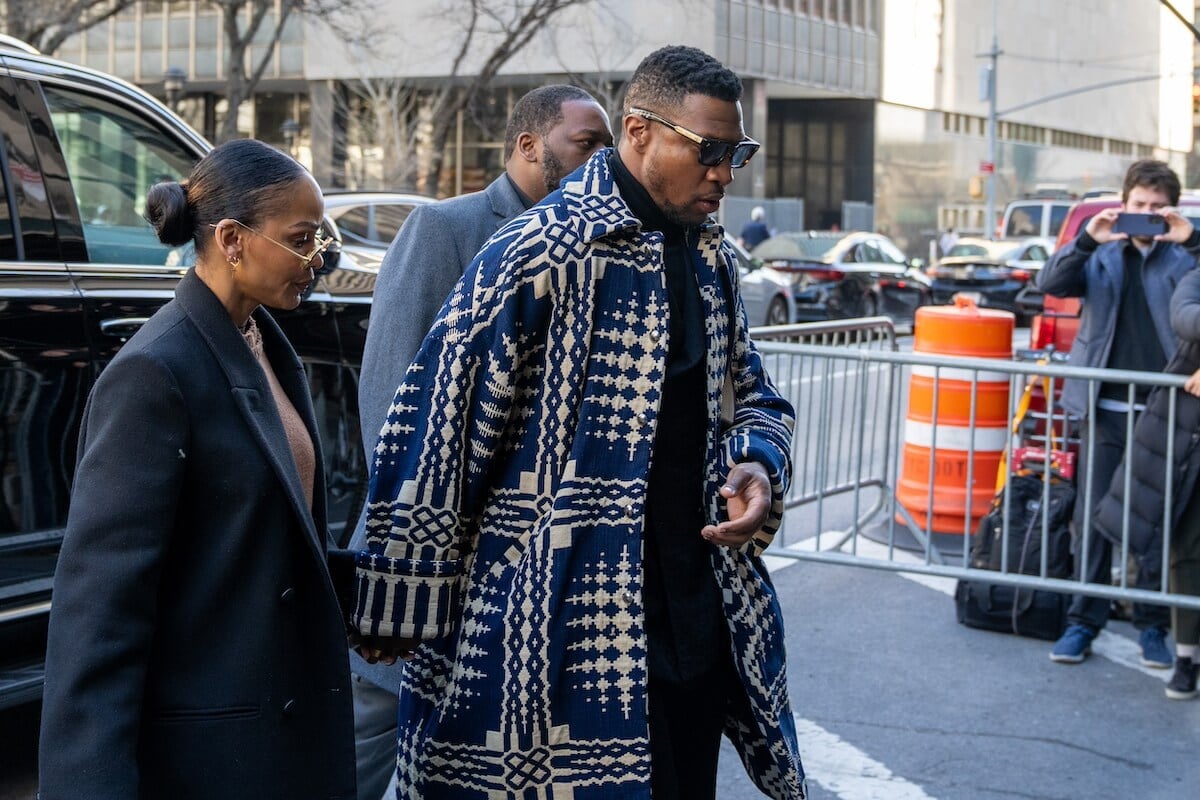 Jonathan Majors, in a patterned coat, holds hands with Meagan Good as they walk into court in NYC