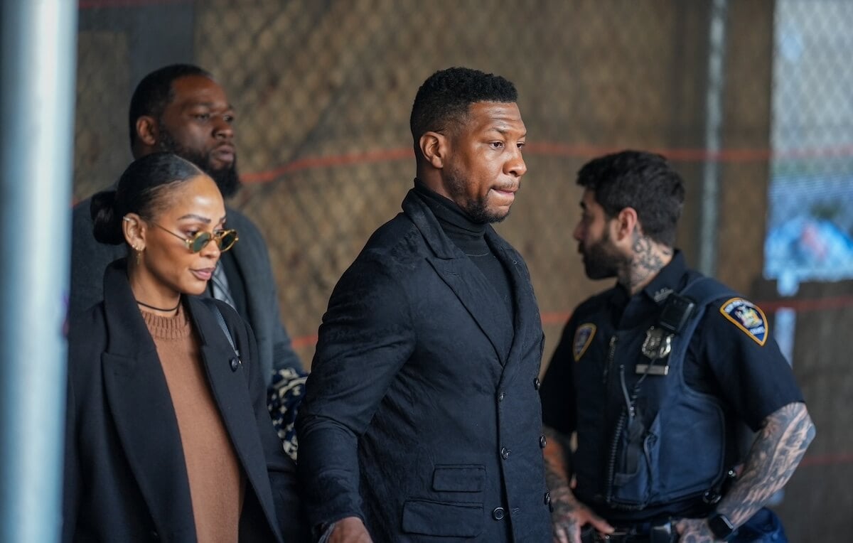 Meagan Good and Jonathan Majors leave court with a police officer in the background