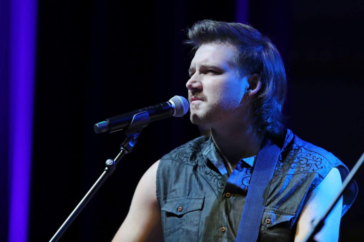 Morgan Wallen wears a sleeveless shirt and stands in front of a microphone.