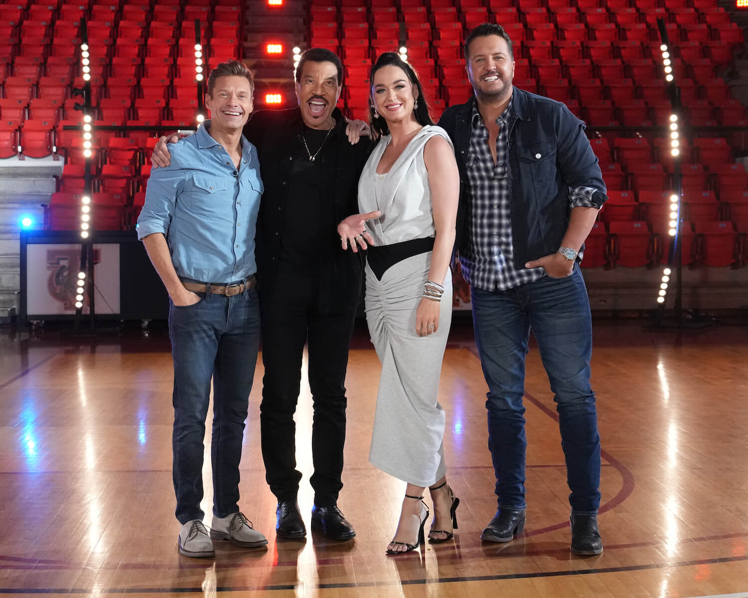 'American Idol' host Ryan Seacrest standing with judges Lionel Richie, Katy Perry, and Luke Bryan on a stage with red seats behind them