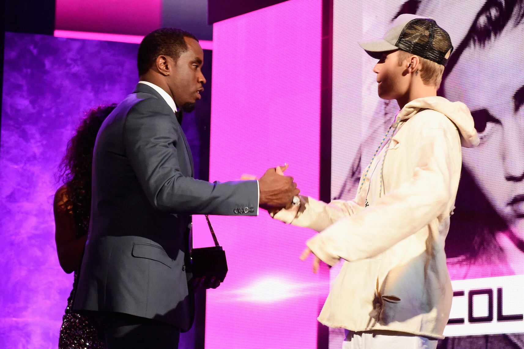 Sean 'P. Diddy' Combs and Justin Bieber shaking hands against a purple background at the 2015 American Music Awards