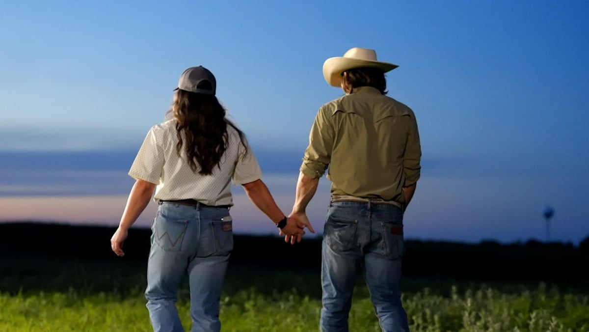 Woman with long hair holding hands with a man in a cowboy hat with their backs to the camera