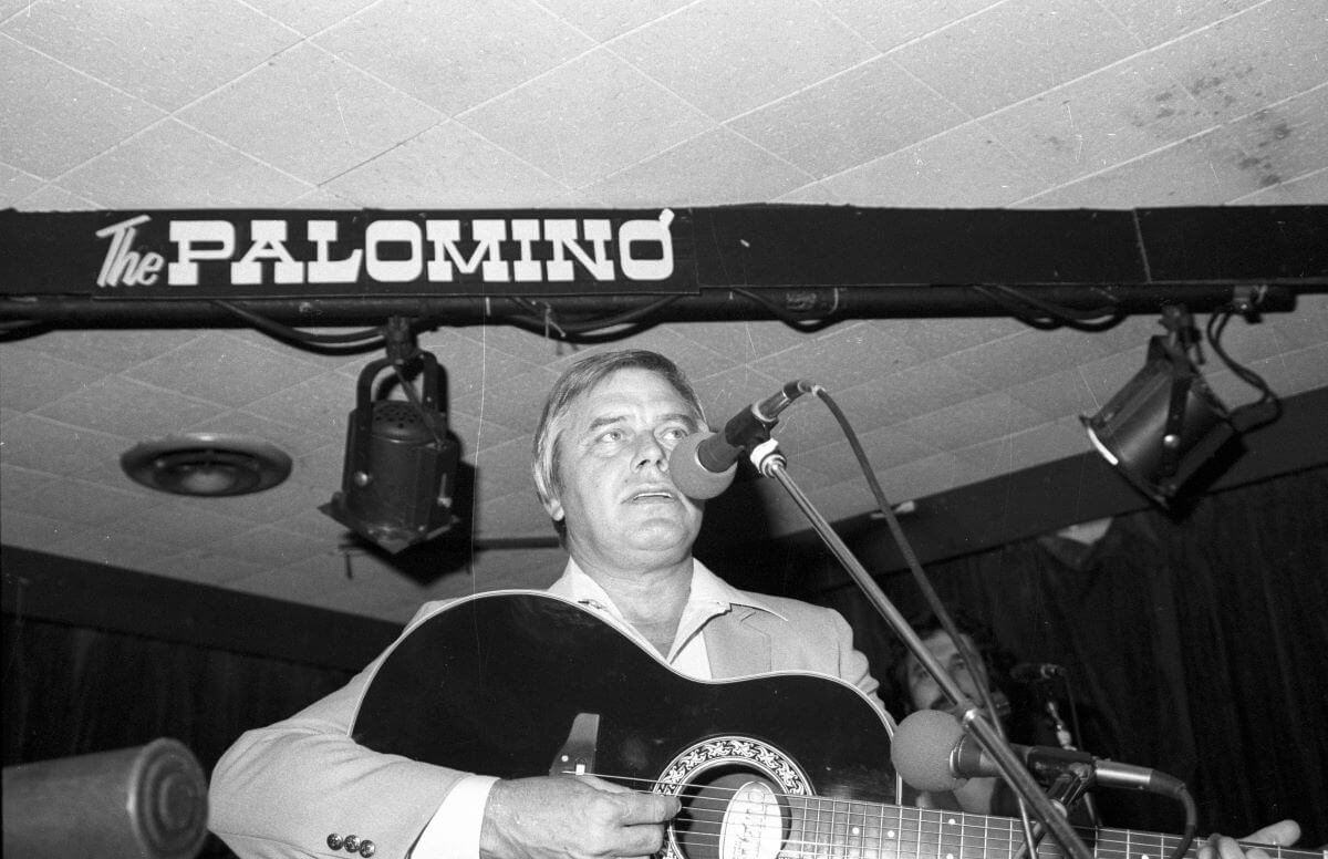 A black and white picture of Tom T. Hall playing an acoustic guitar and singing into a microphone.