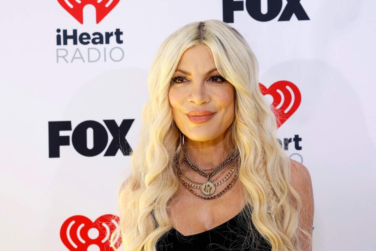 Wearing a black tank top and plaid pants, Tori Spelling smiles for cameras at the 2024 iHeartRadio Music Awards