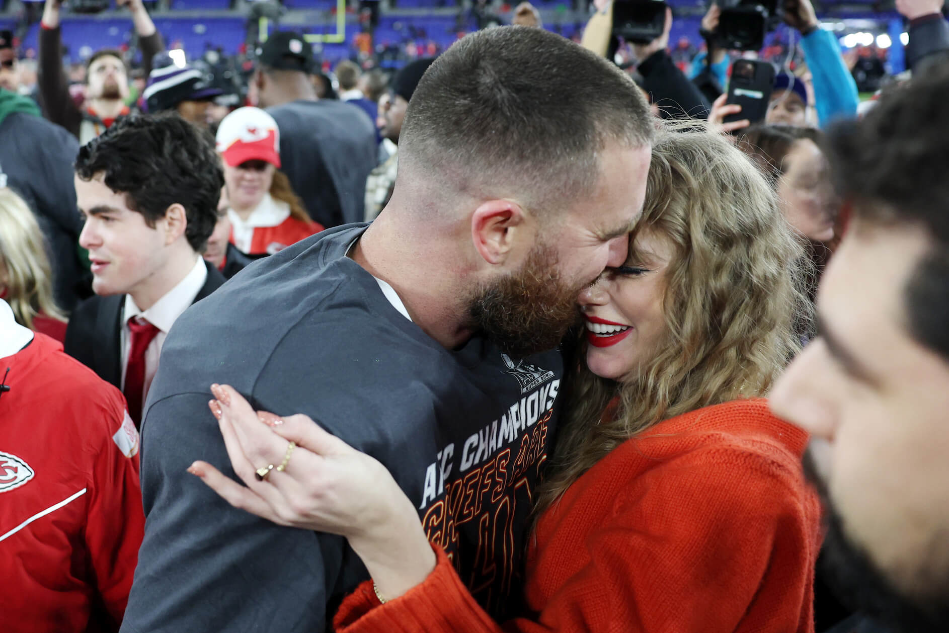 Travis Kelce tightly hugging Taylor Swift among a crowd oe people after a Kansas City Chiefs football game