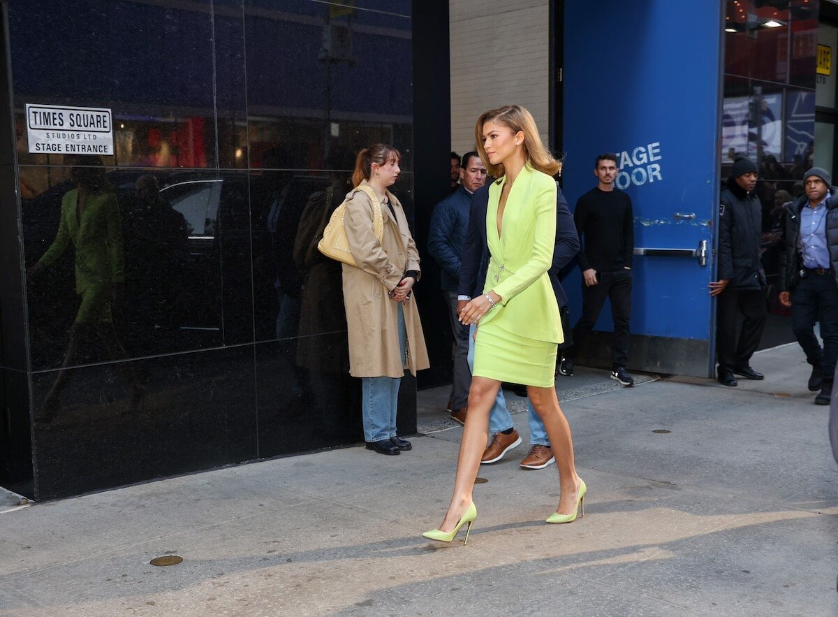 Zendaya walks by a stage door in a green suit