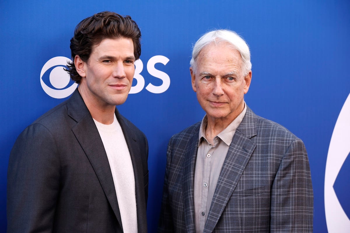 Austin Stowell and Mark Harmon pose for a photo in front of blue CBS backdrop