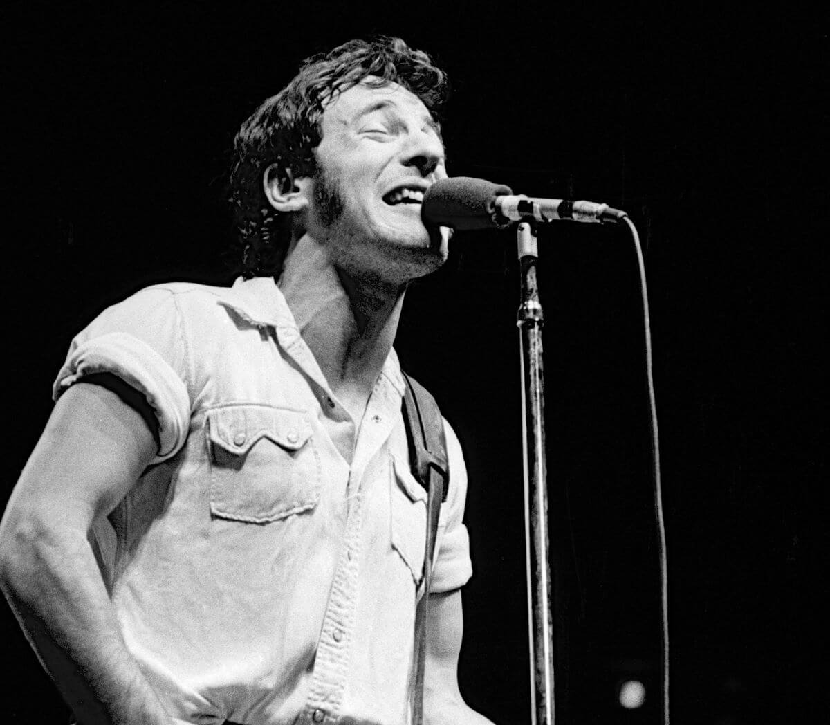 A black and white picture of Bruce Springsteen singing into a microphone.