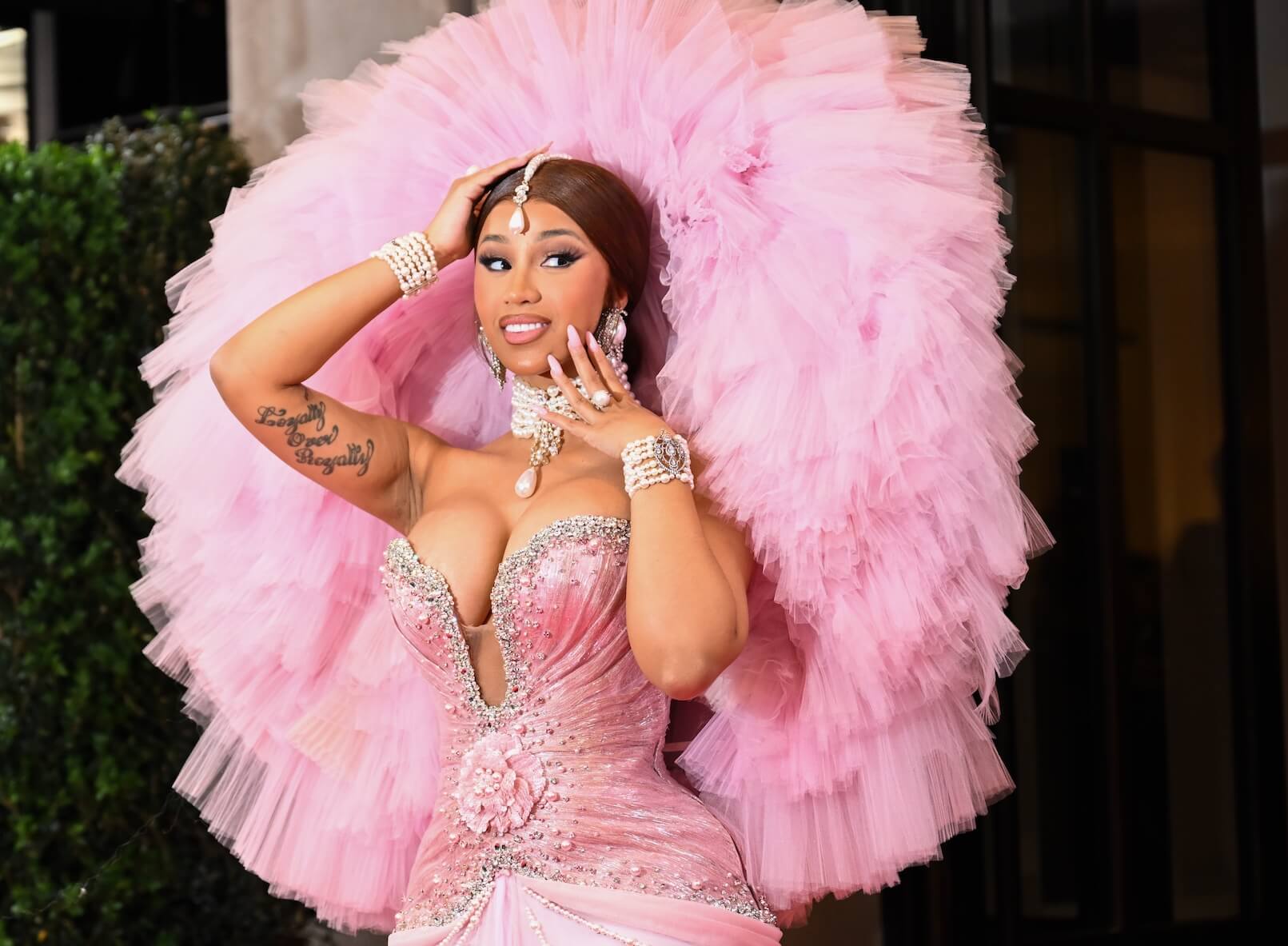Cardi B posing for the Met Gala 2023. She's wearing a pink dress with a tight bodice and a light pink tulle head and back piece.