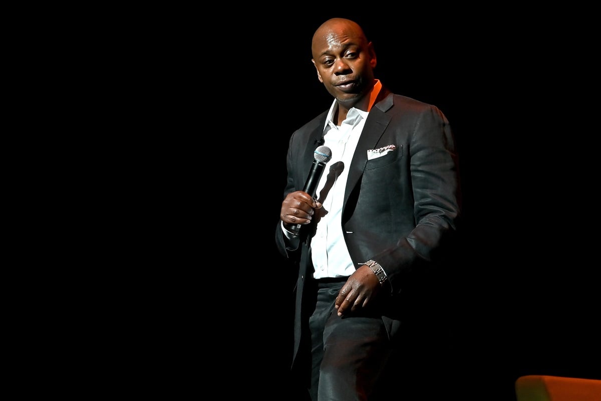 Dave Chappelle performing on stage wearing a suit.