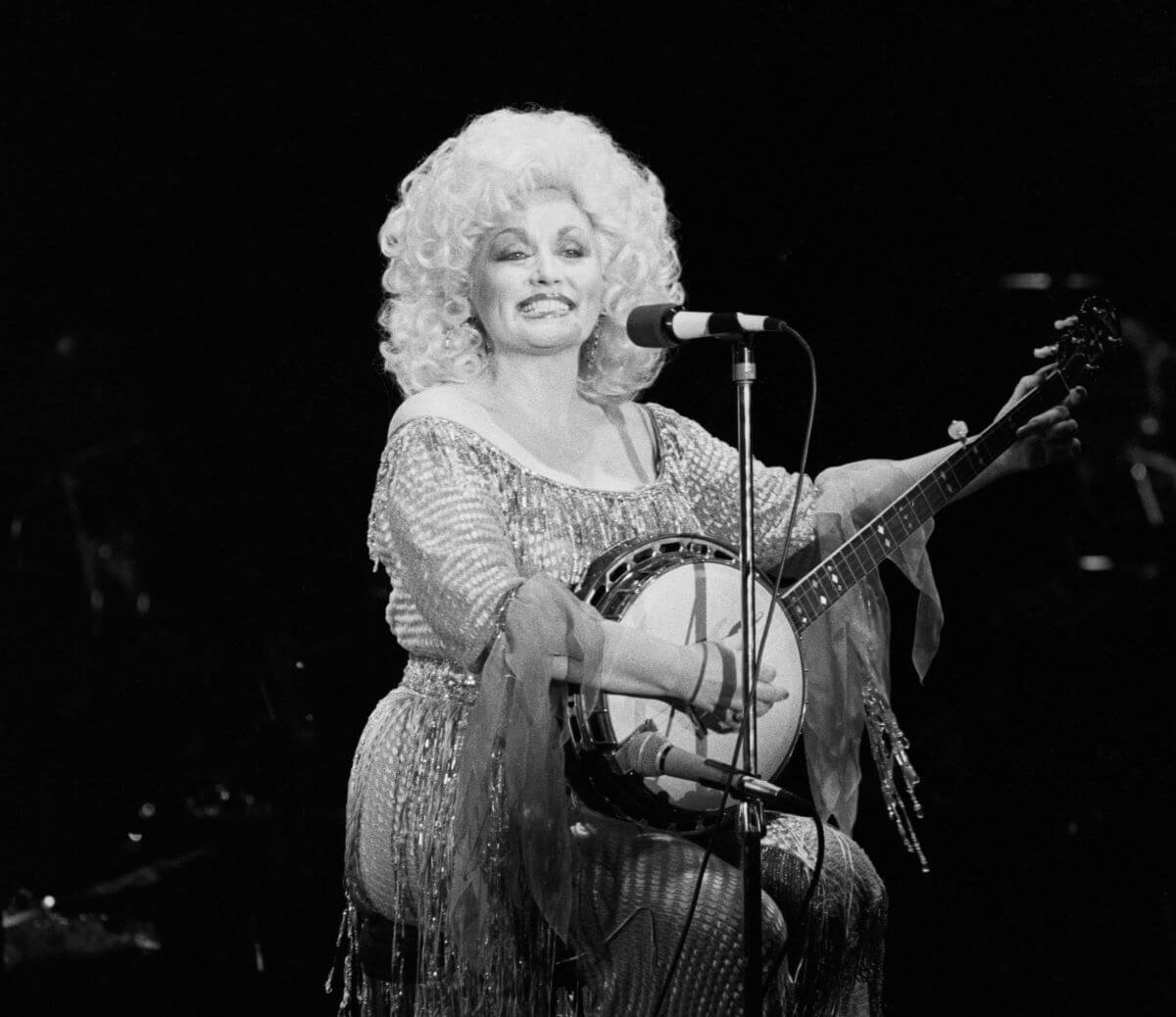 A black and white picture of Dolly Parton sitting while playing the banjo.