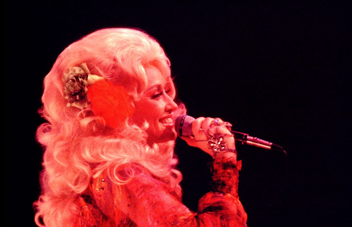 Dolly Parton sings into a microphone. She wears a flower in her hair.