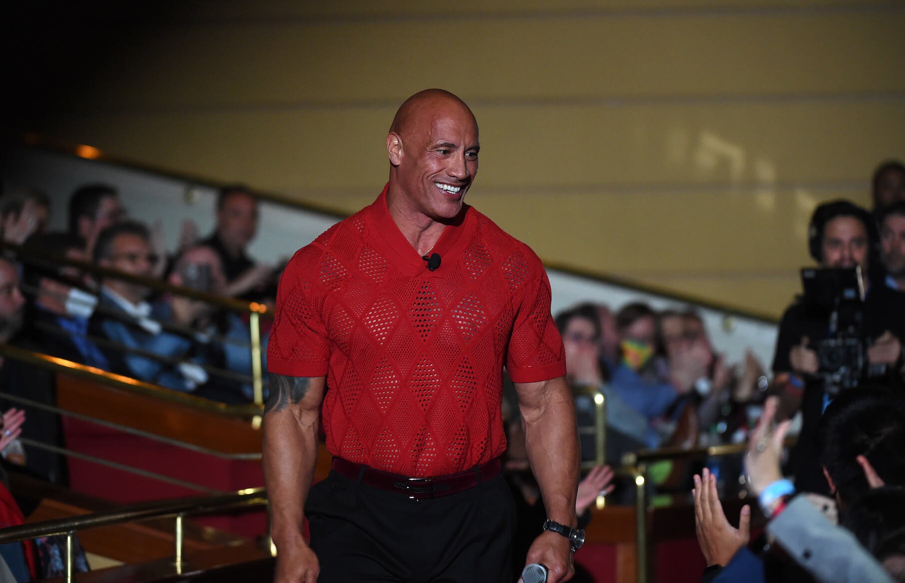 Dwayne 'The Rock' Johnson smiling with a crowd in the background in 2022. He's wearing a red T-shirt.