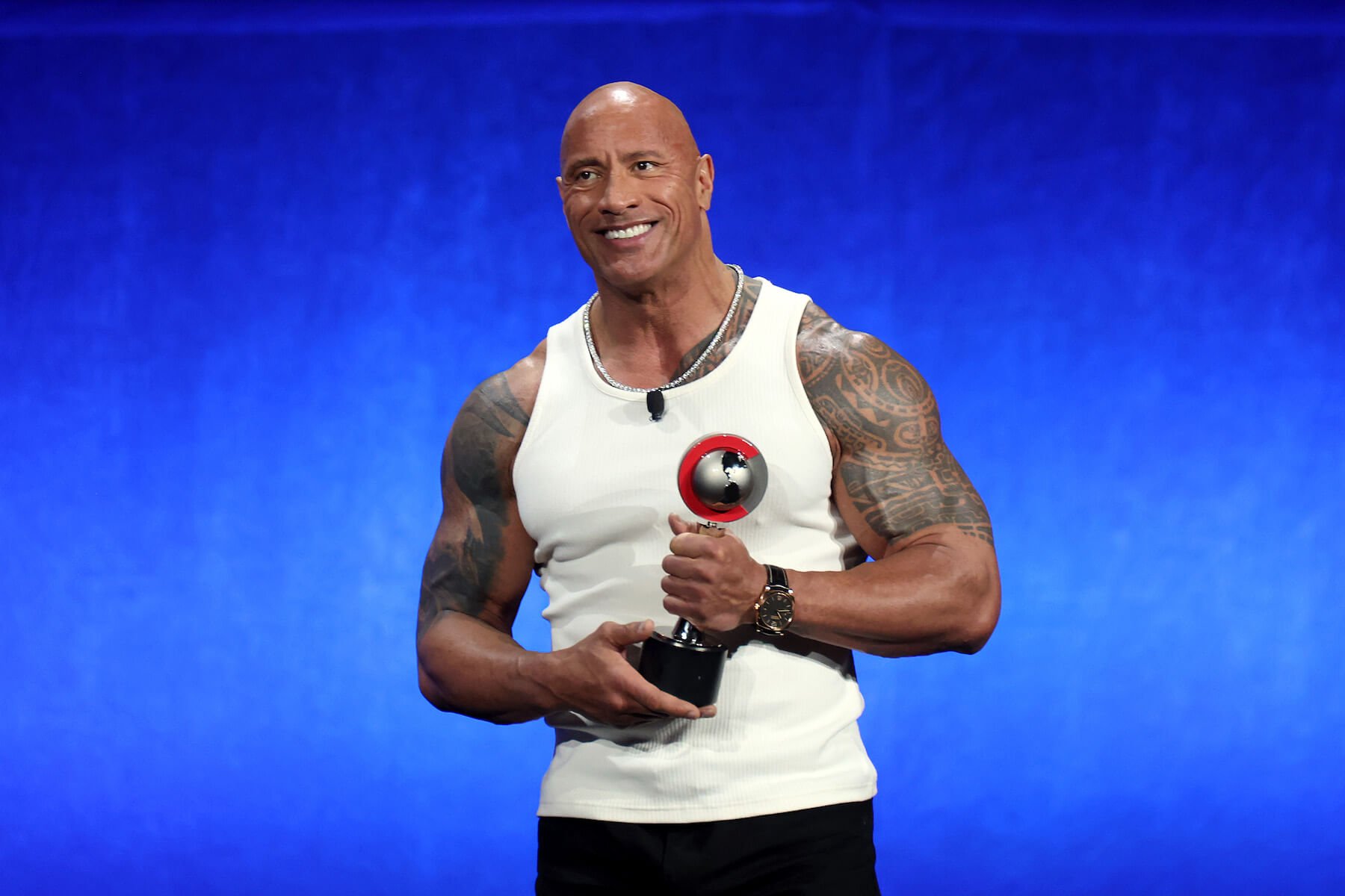 Dwayne 'The Rock' Johnson smiling while accepting an award against a blue background in 2024