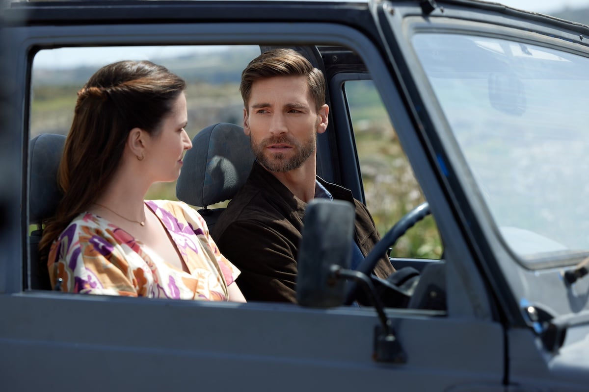 Man and woman sitting in a jeep and looking at each other in the Hallmark movie 'For Love and Honey'