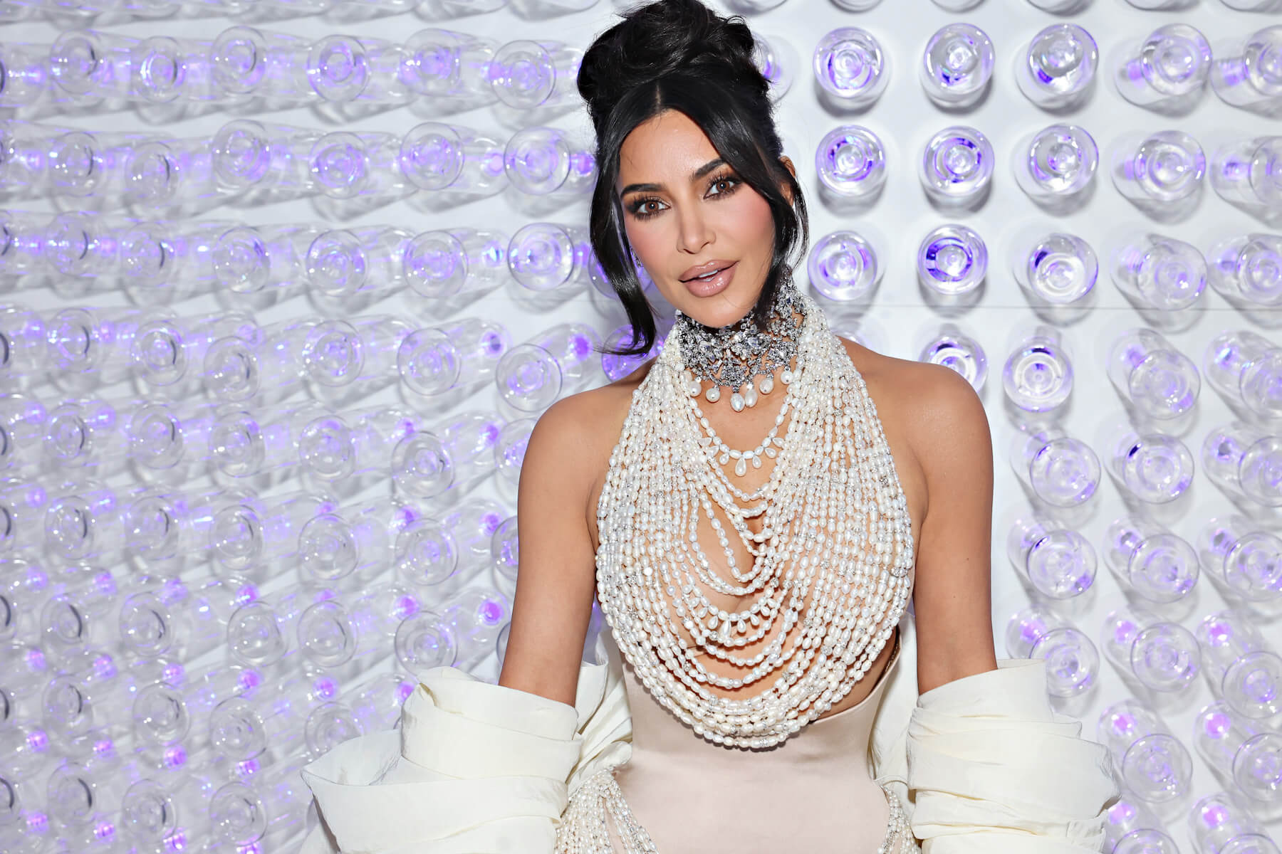 Kim Kardashian wearing a pearl dress and standing against a purple background at the 2023 Met Gala