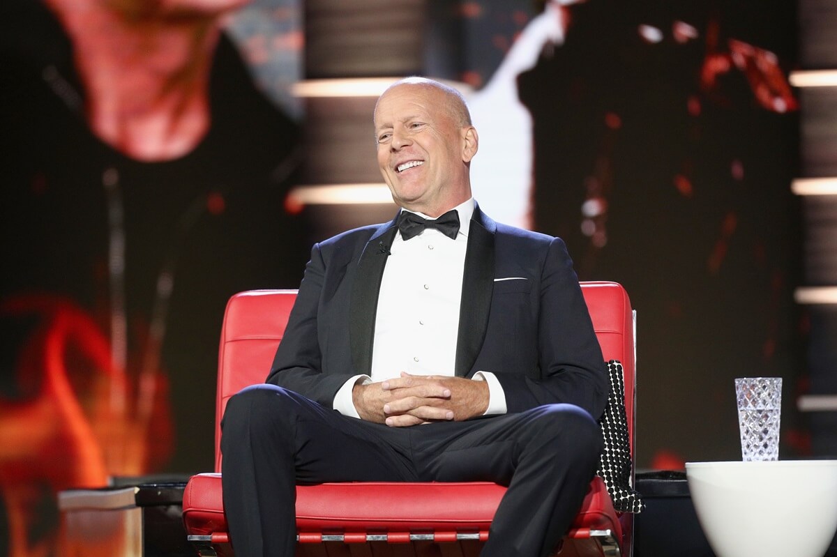 Bruce Willis sitting down in a suit at the comedy central roast of Bruce Willis.