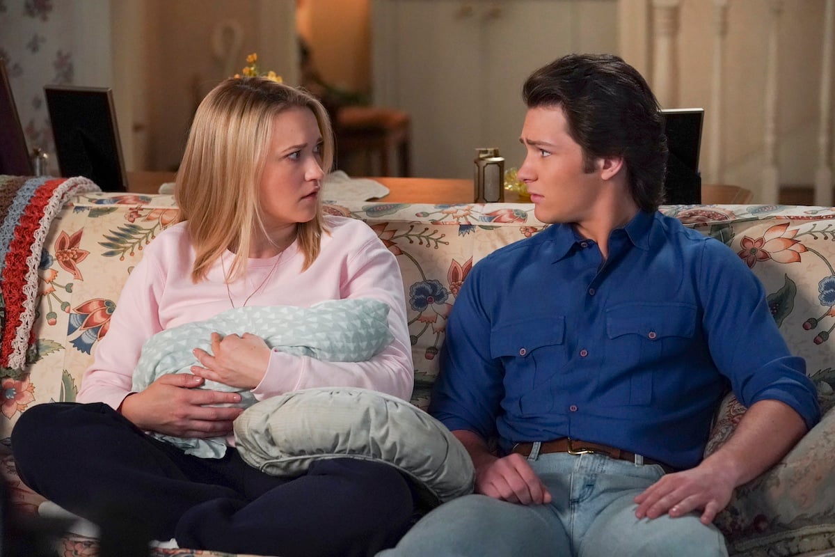 Mandy, holding her baby, sitting next to Georgie on a couch in 'Young Sheldon'