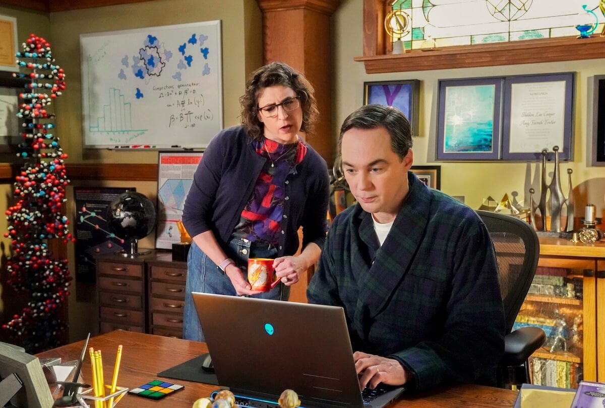 Mayim Bialik holding a coffee mug looking over Jim Parsons' shoulder at his laptop screen in the 'Young Sheldon' series finale
