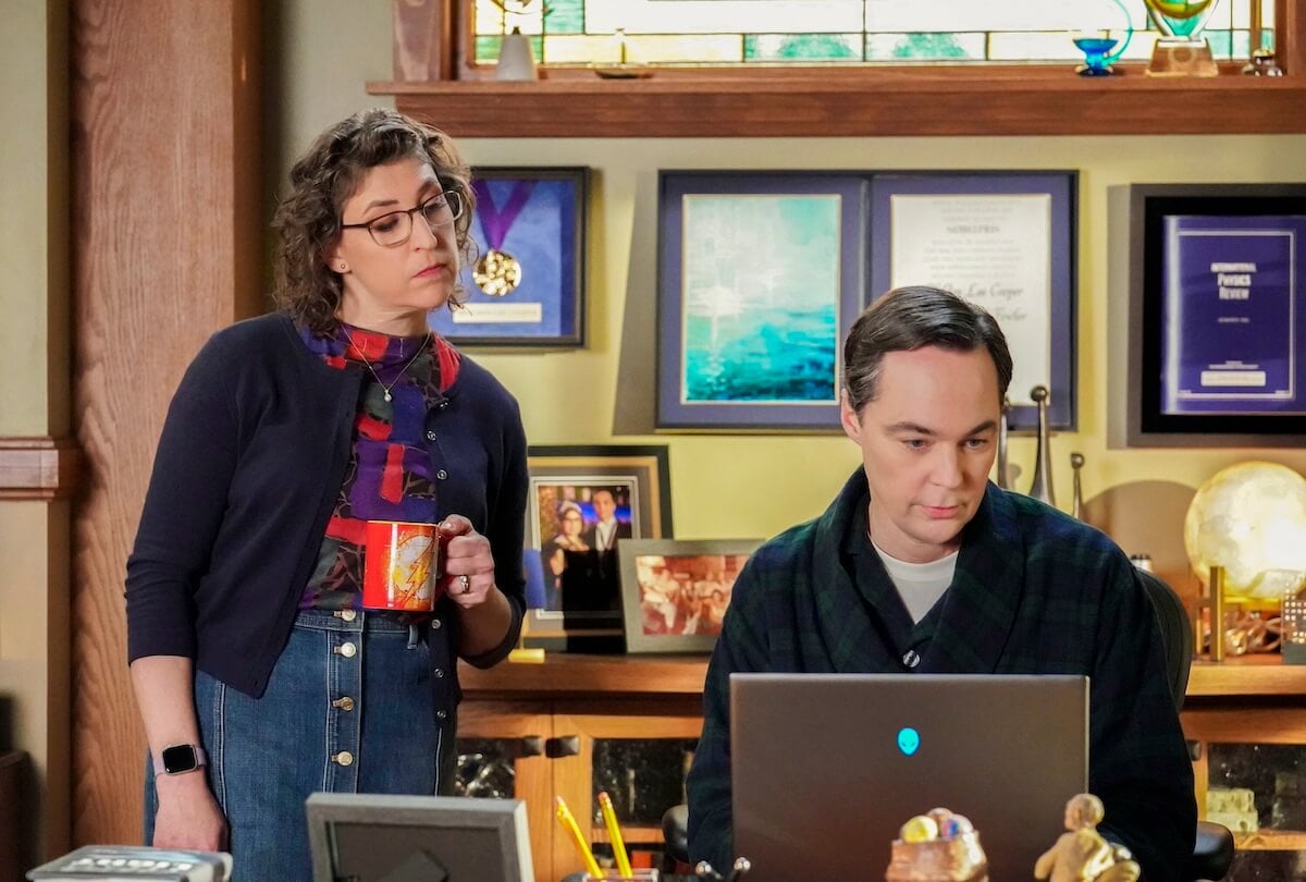 Mayim Bialik holding a coffee mug looking over Jim Parsons' shoulder at his laptop screen in the 'Young Sheldon' series finale