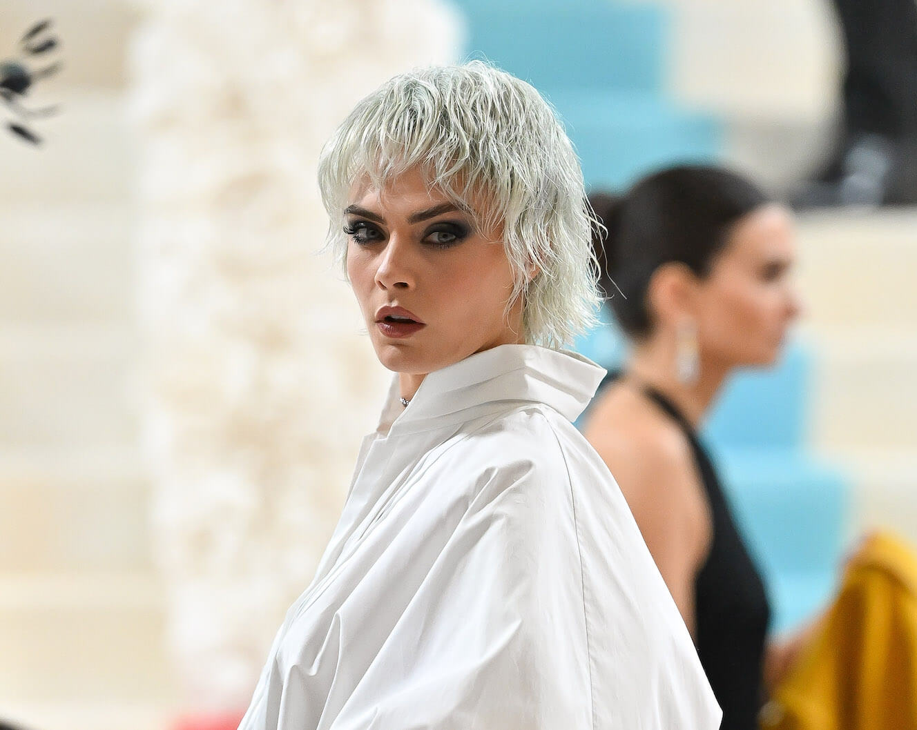 A close up of Cara Delevingne at the 2023 Met Gala. Her hair is bleached white-blonde, and she's wearing a white shirt.