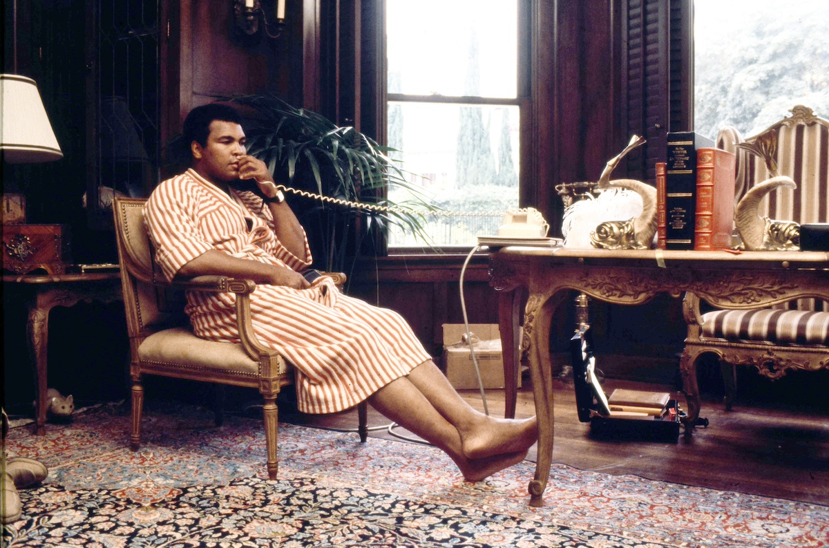 Muhammad Ali in a robe, sitting in a chair and talking on the phone in 1980