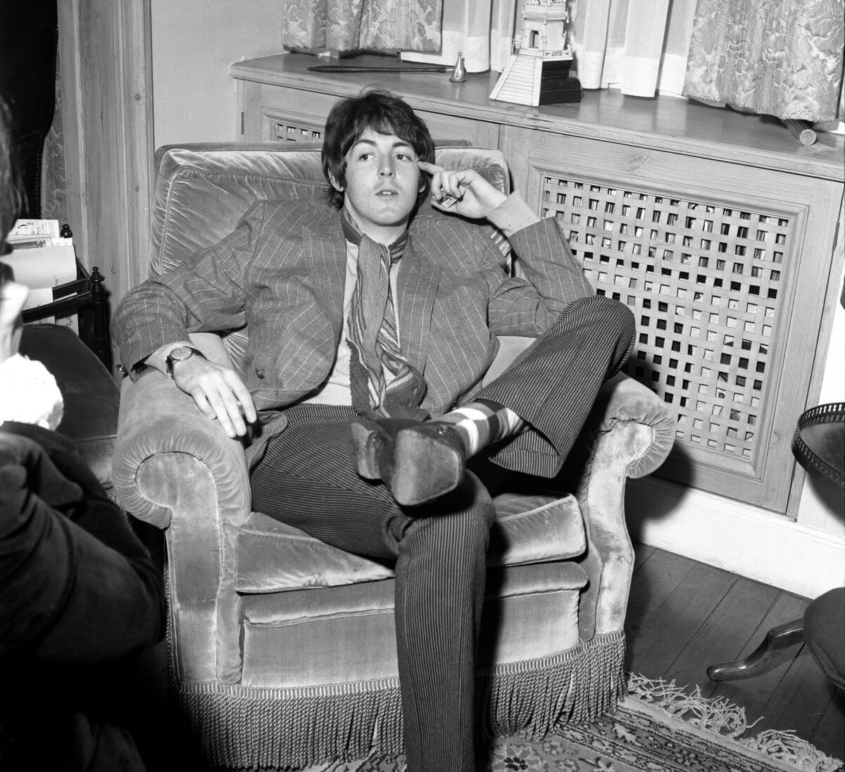 A black and white picture of Paul McCartney sitting in an arm chair with one leg folded over the other.
