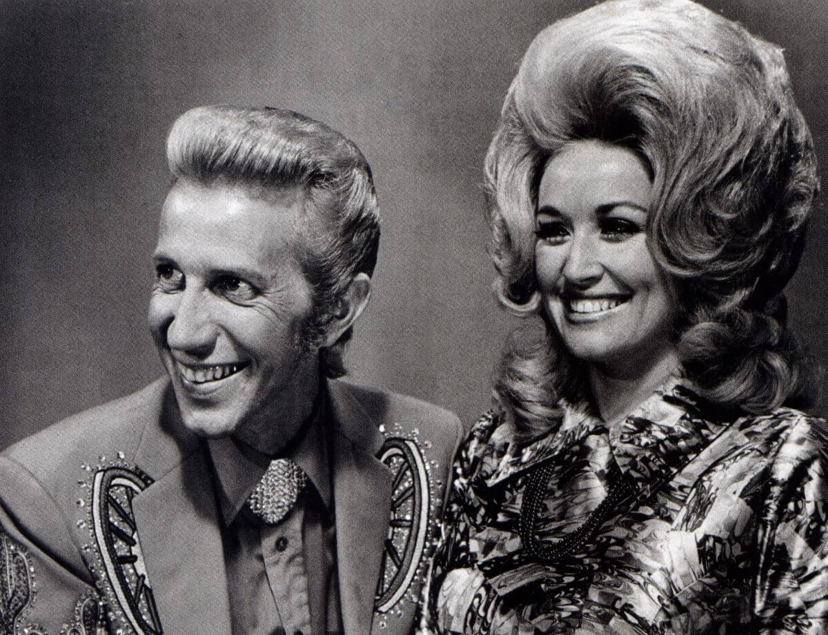 A black and white picture of Porter Wagoner and Dolly Parton smiling together.