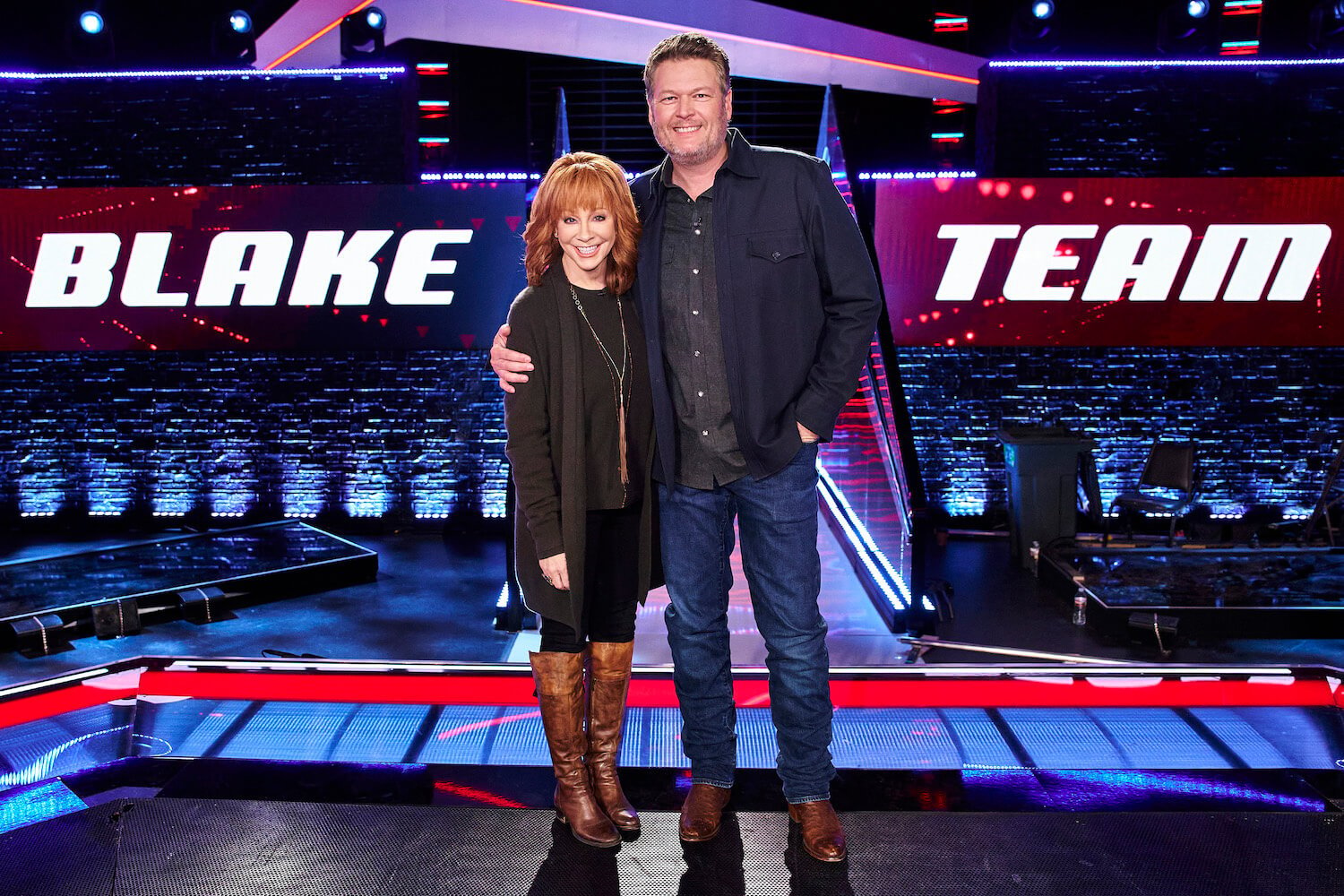 Reba McEntire hugging Blake Shelton on the set of 'The Voice.' There is a 'Blake Team' sign behind them.