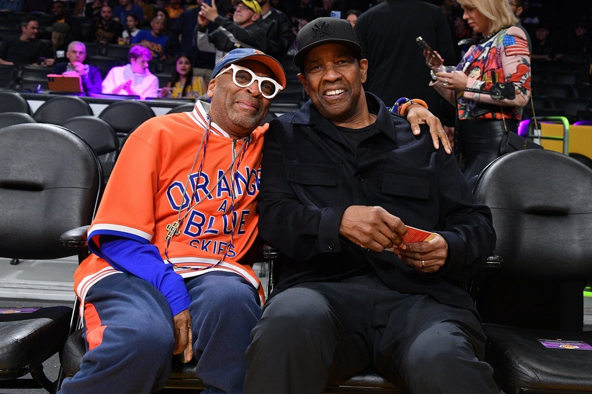 Spike Lee smiling next to Denzel Washington while the two are at a basketball game.