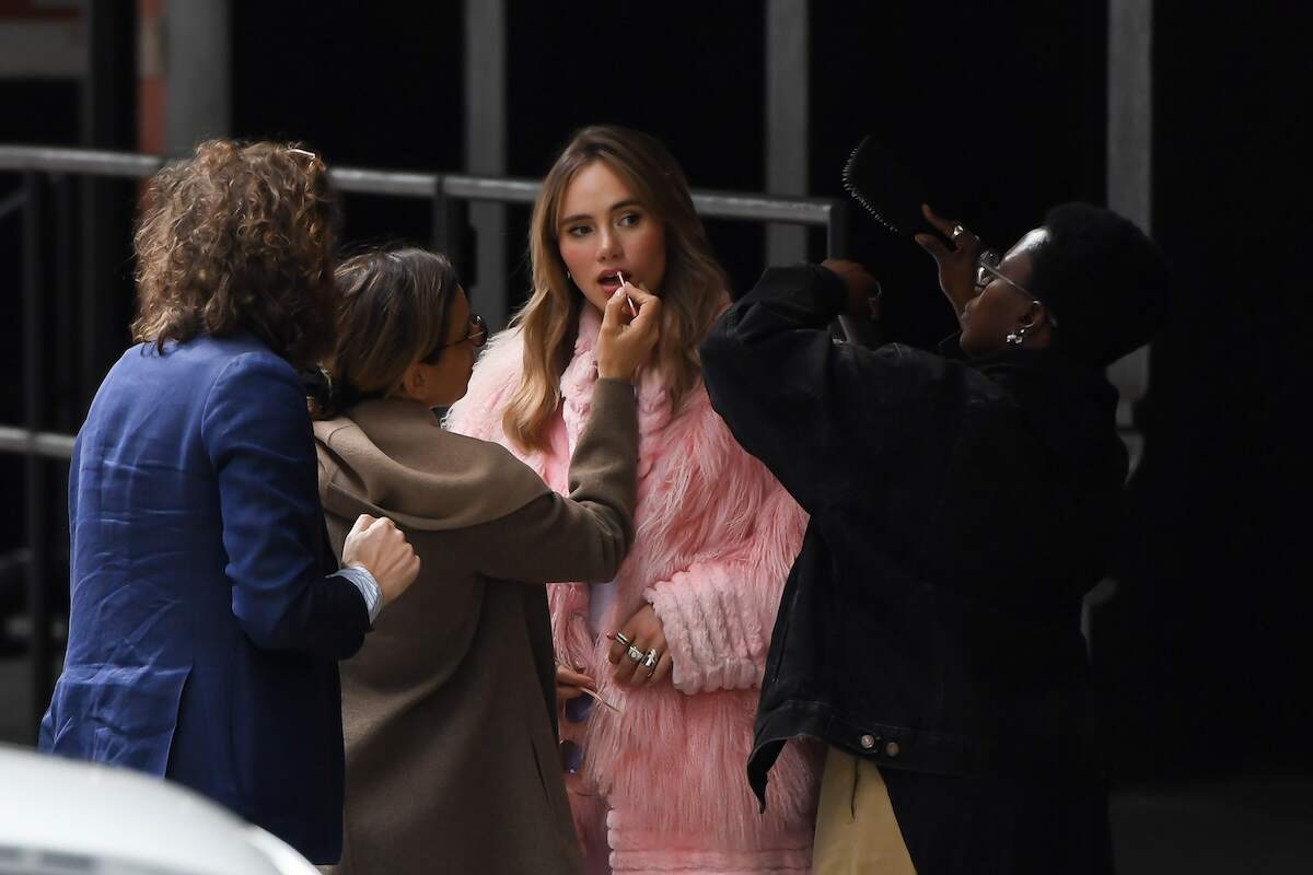 Actor/singer Suki Waterhouse wears a fluffy pink coat and applies lipstick