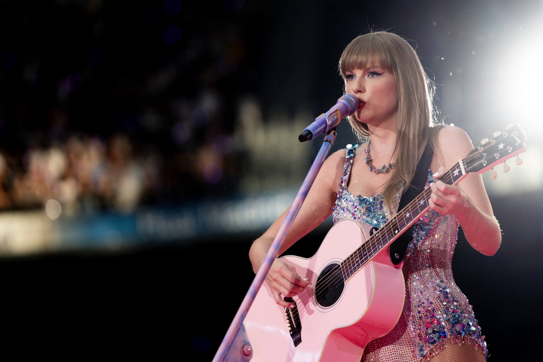 Taylor Swift singing into a microphone and playing guitar during 'The Eras Tour' in Madrid, Spain