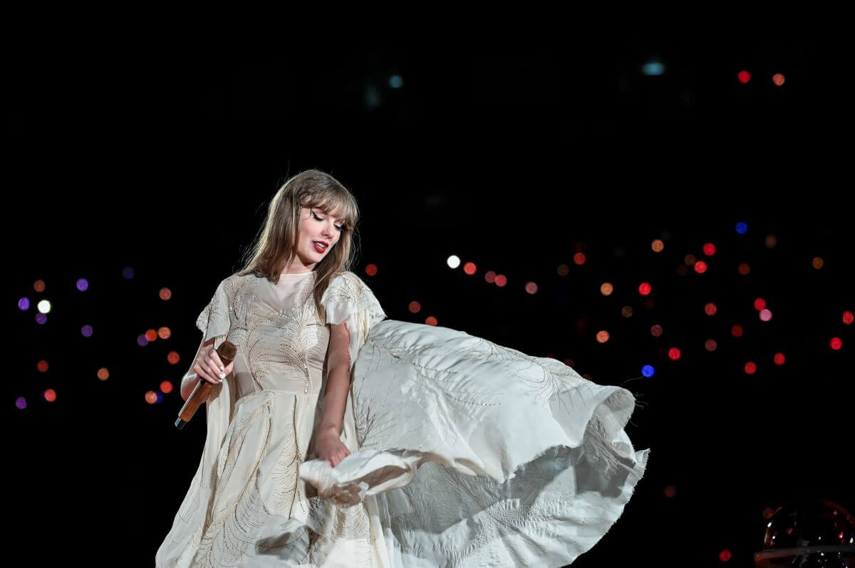 Taylor Swift holds a microphone and wears a flowing white dress.
