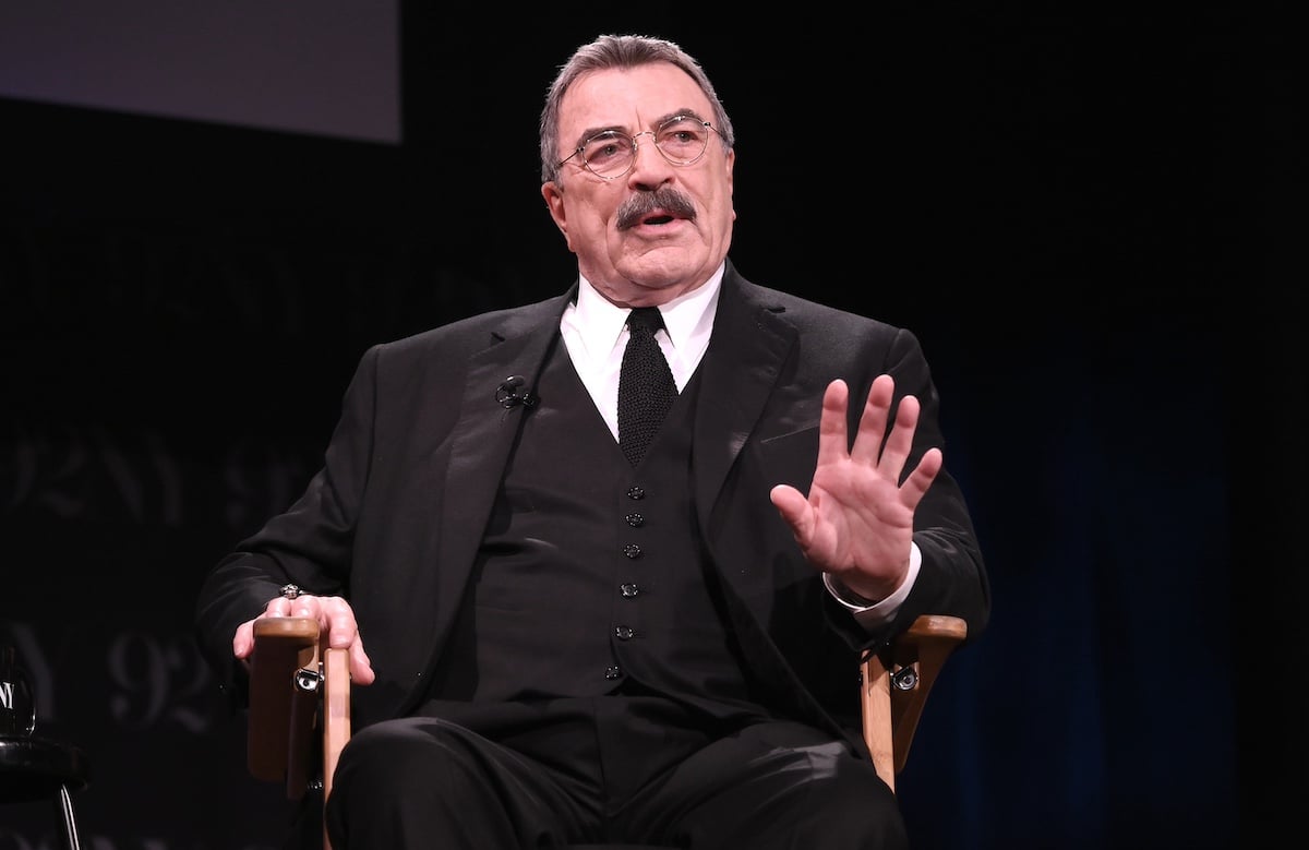 Tom Selleck in a black suit and sitting on stage