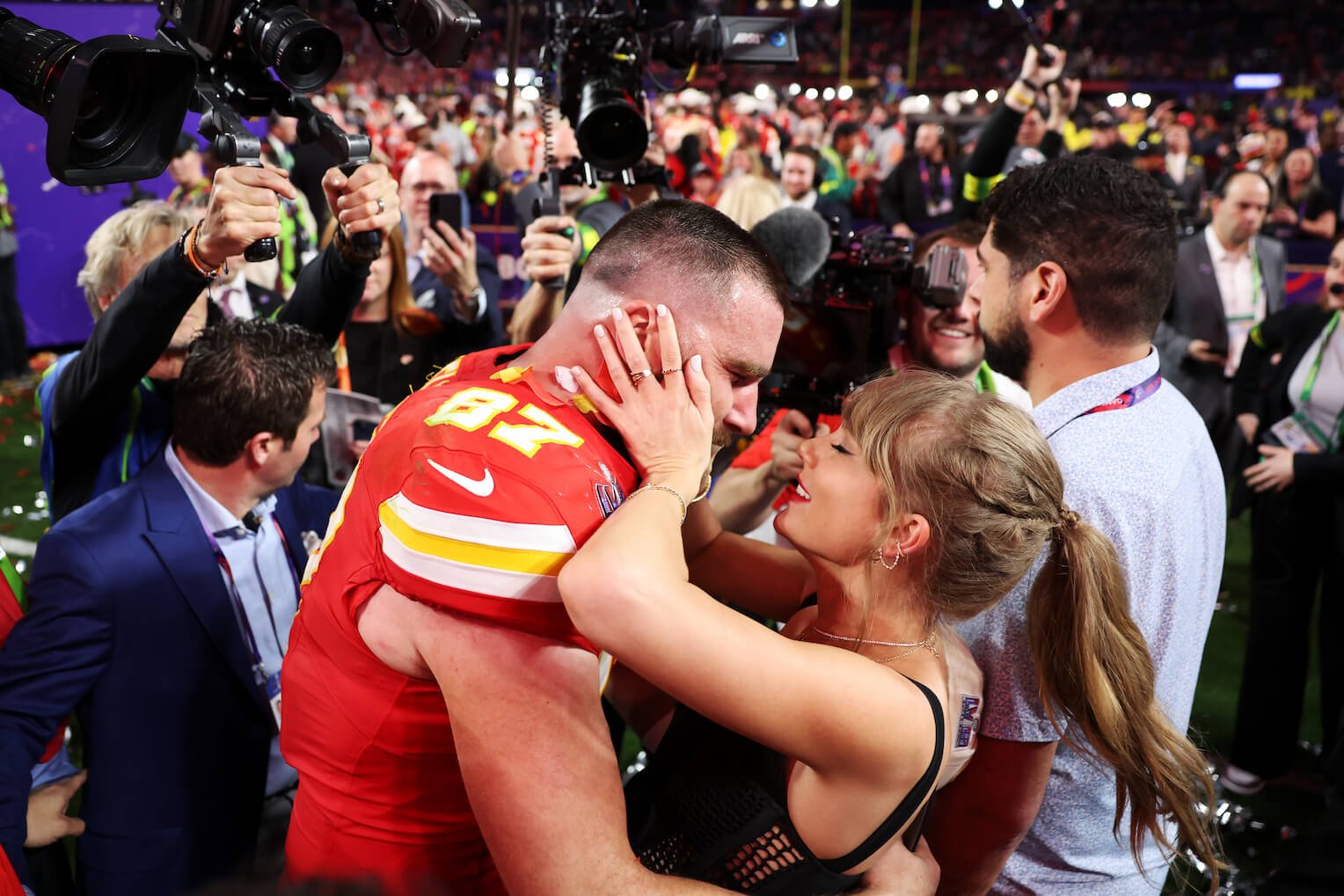 Taylor Swift holding Travis Kelce's face after the Super Bowl in 2024. They're surrounded by a large crowd.
