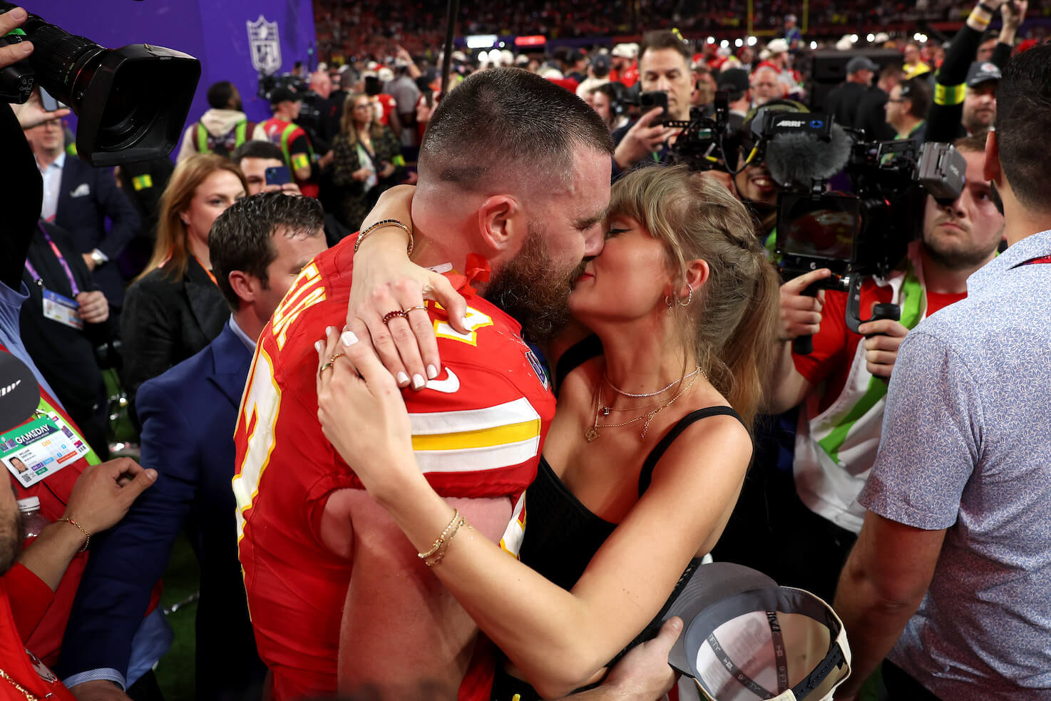 Travis Kelce kissing Taylor Swift while in his Kansas City Chiefs uniform and surrounded by a crowd