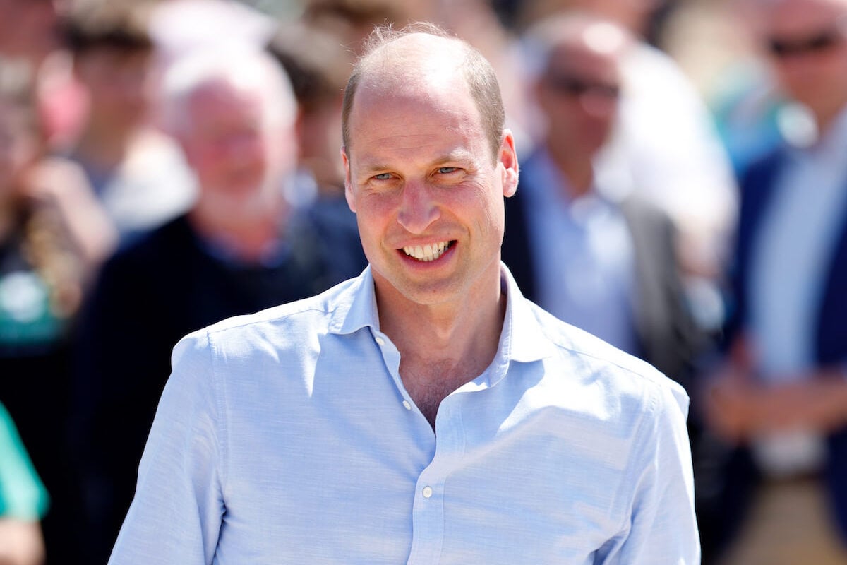 Prince William, who is doing the Japanese state visit greeting without Kate Middleton, smiles wearing a blue collared shirt.