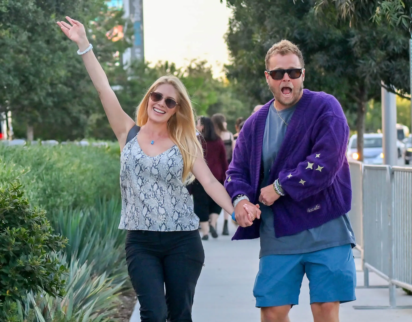 Heidi Montag and Spencer Pratt walking in Los Angeles. Montag has one arm up while she holds Pratt's hand. Pratt is making a funny face at the camera.