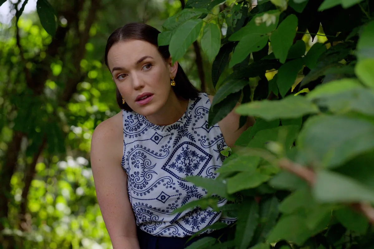 Woman hiding in the bushes in Hallmark movie 'Mystery Island: Play for Keeps'