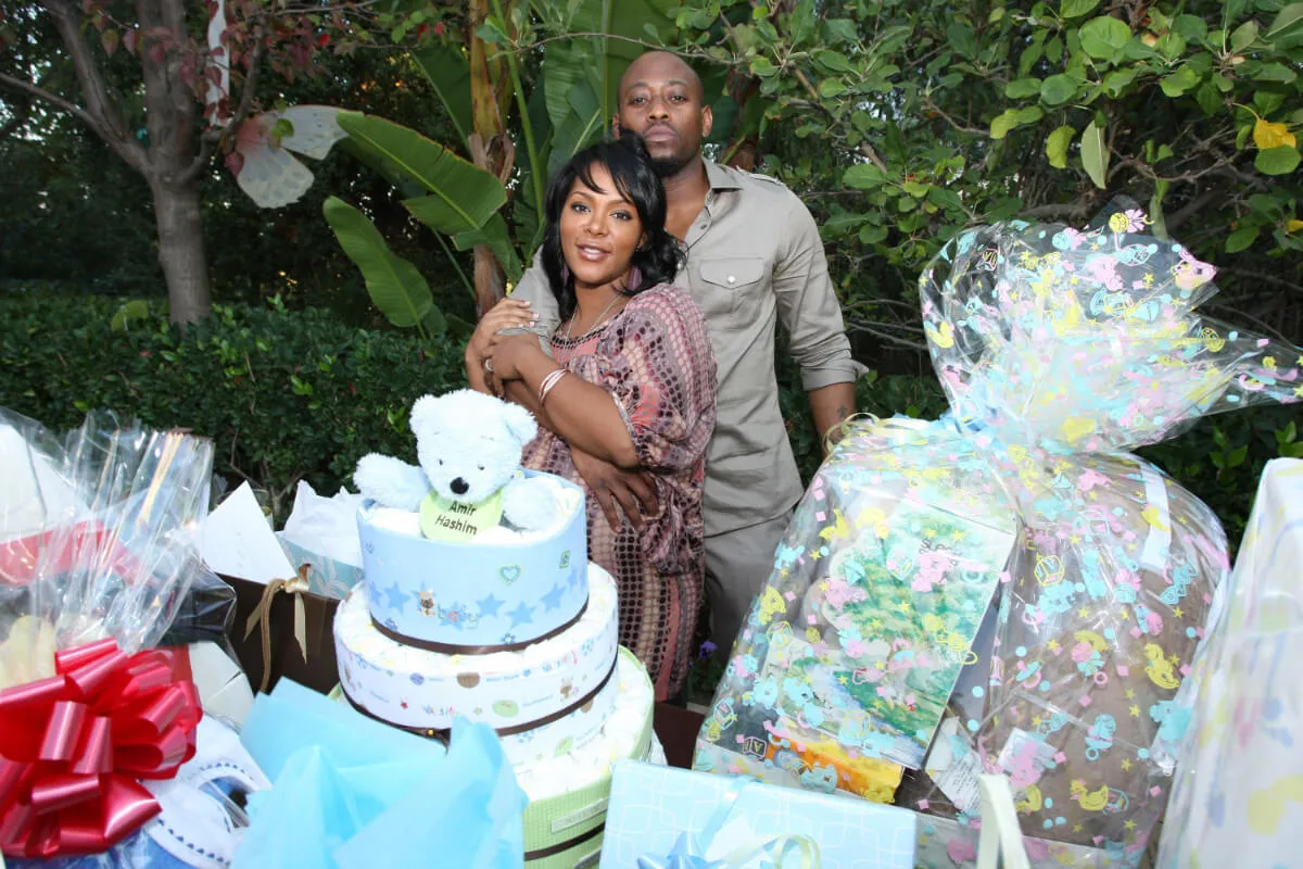 Omar Epps and Keisha Spivey stand in front of a table with cake and presents at a baby shower.