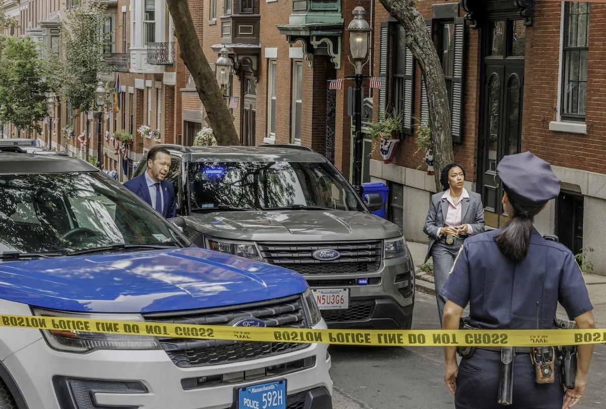 Donnie Wahlberg and Sonequa Martin-Green standing behind yellow police tape in 'Boston Blue' series premeire