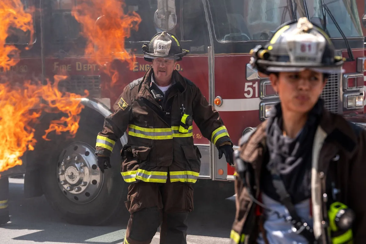 Man and woman in firefighting gear in front of a burning fire truck in 'Chicago Fire' Season 14 premiere