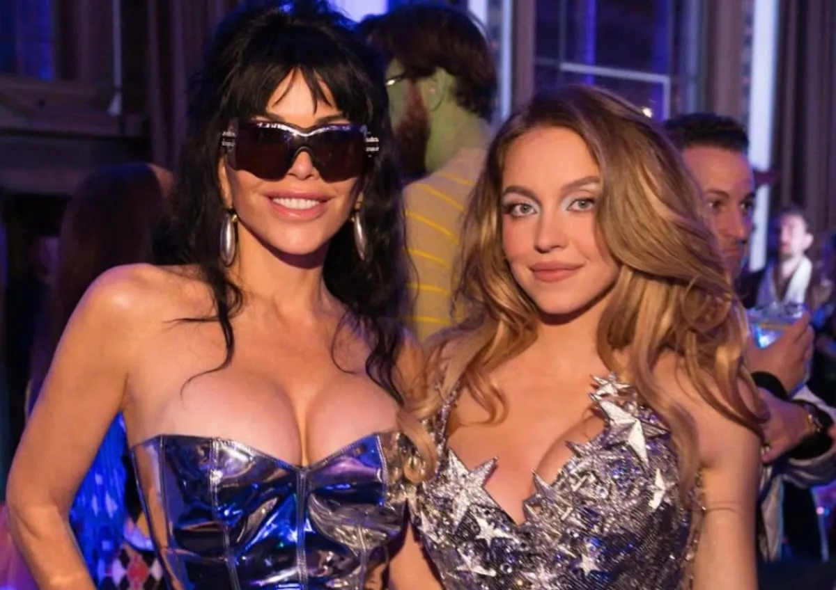 Both wearing silver dresses, Sydney Sweeney smiles with Lauren Sanchez Bezos