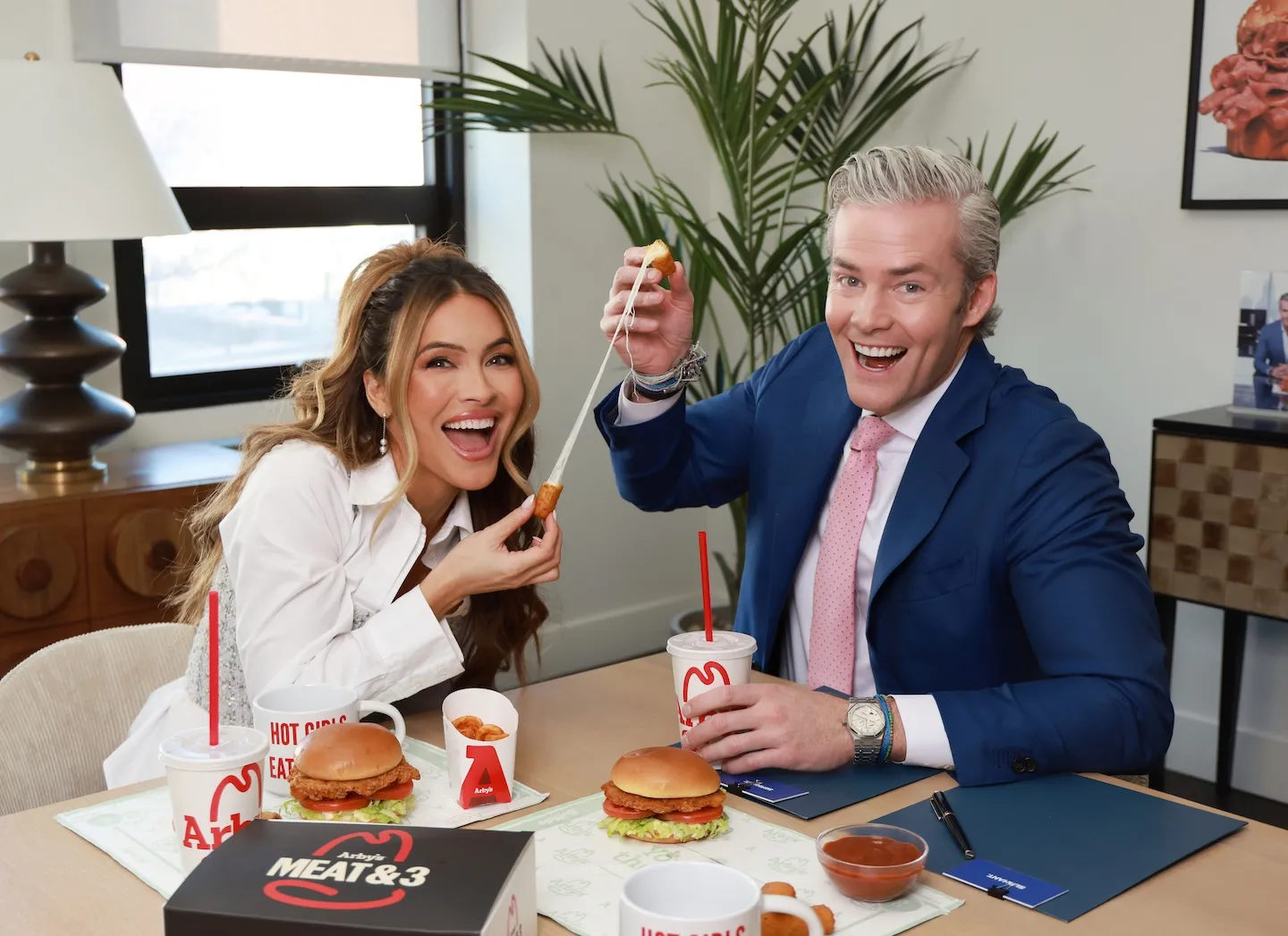 Ryan Serhant and Chrishell Stause pulling apart a mozzarella stick while smiling toward the camera for an Arby's campaign