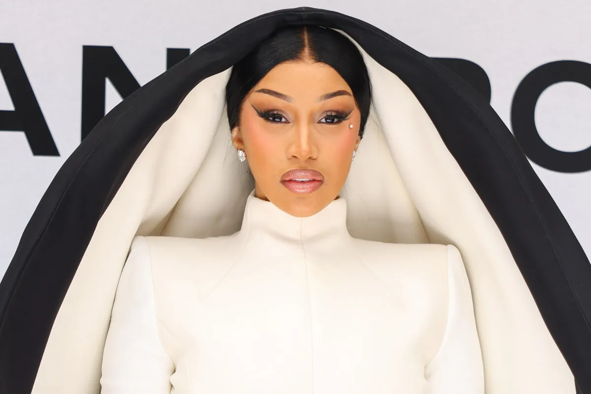 Cardi B wears a white turtleneck with an oversized black and white hood.
