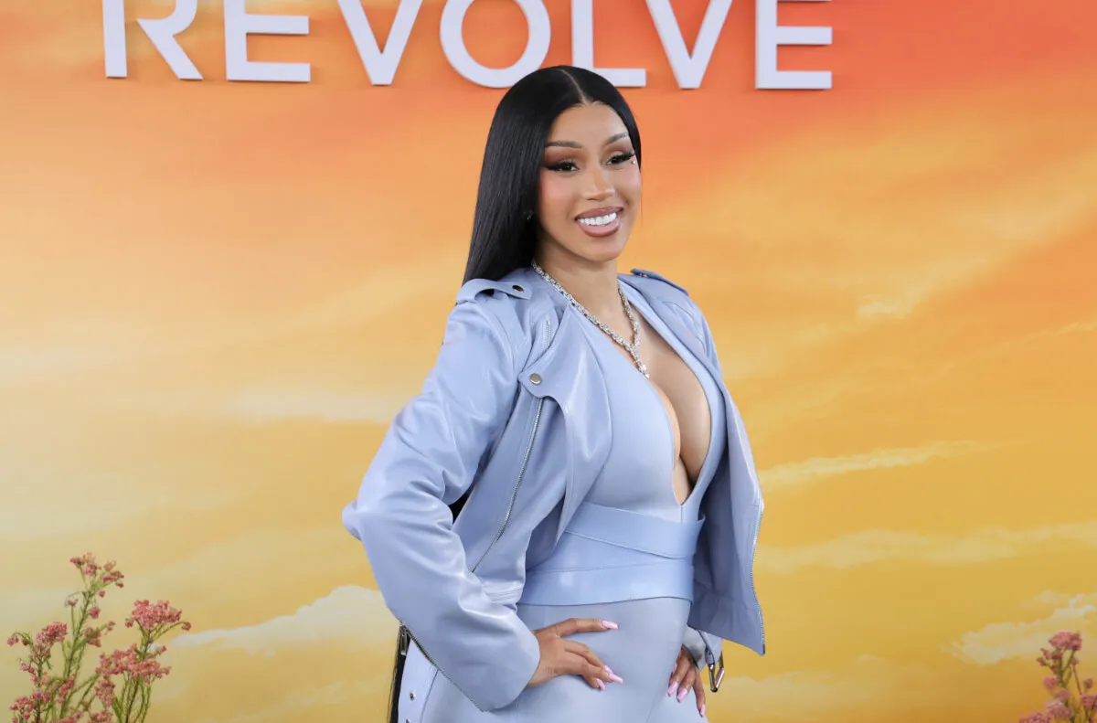 Cardi B wears a light blue jacket and jumpsuit. She stands with her hands on her hips.